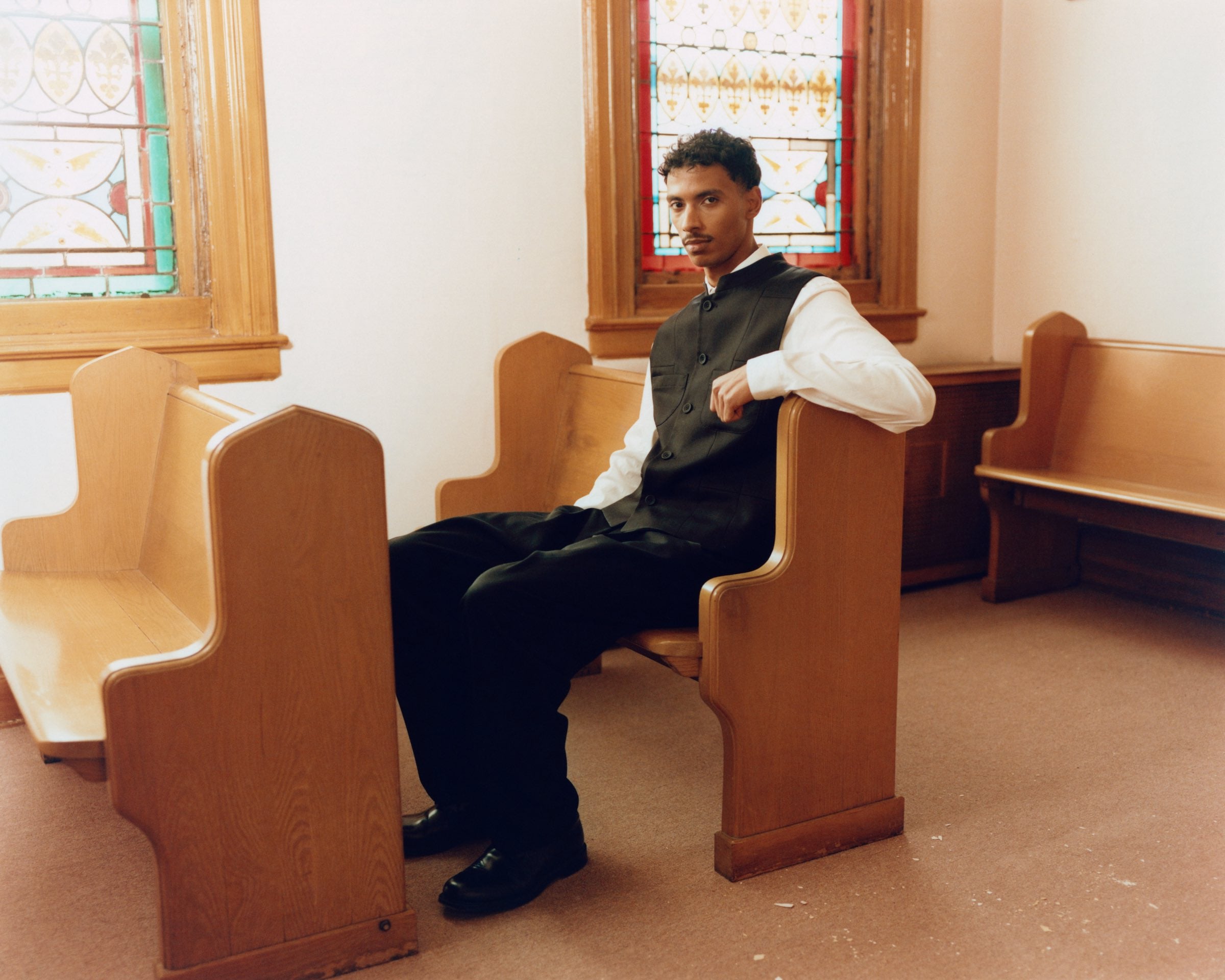 Dark waistcoat and white shirt, seated on a church pew